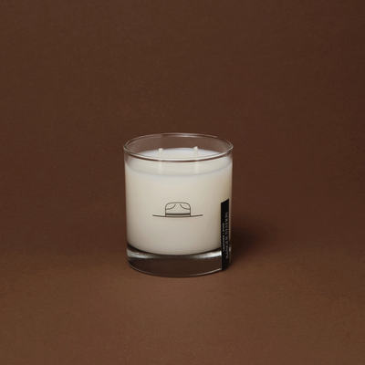 White candle in a glass container with a label on a brown background