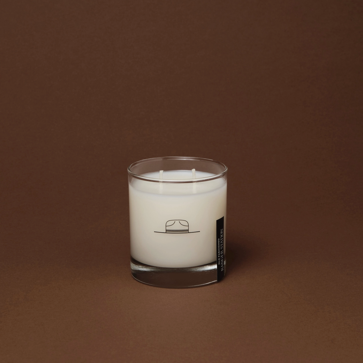 White candle in a glass container with a label on a brown background