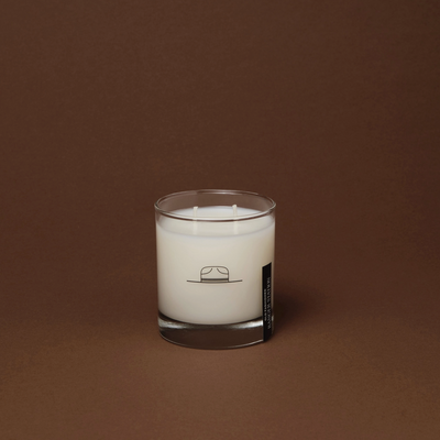 White candle in a glass container with a label on a brown background